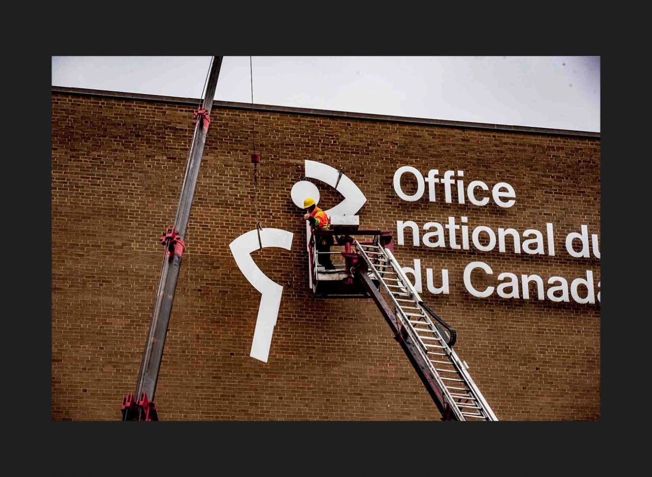 Workers on a lift removing a large NFB symbol from a brick facade