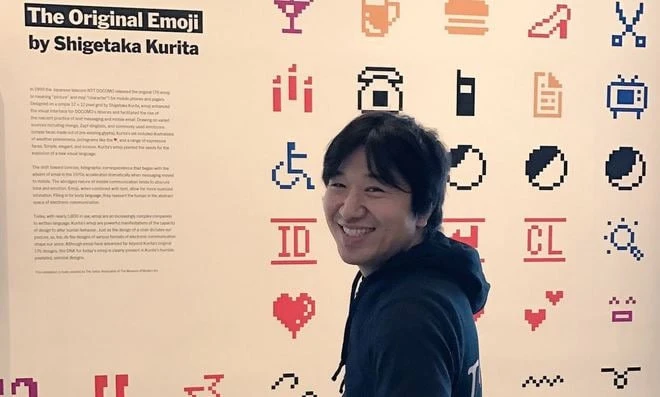 Shigetaka Kurita smiling in front of a panel labelled The Original Emoji and enlarged pictograms.