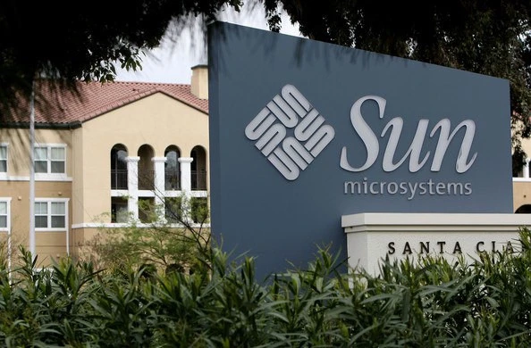 Синьо-сіра вивіска з ромбоподібним знаком Sun Microsystems і великим похилим написом Sun біля будівлі.