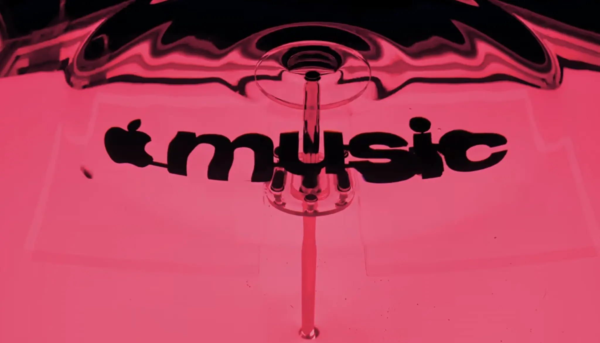 A close-up of black Apple Music lettering distorted by liquid ripples under bright pink lighting.