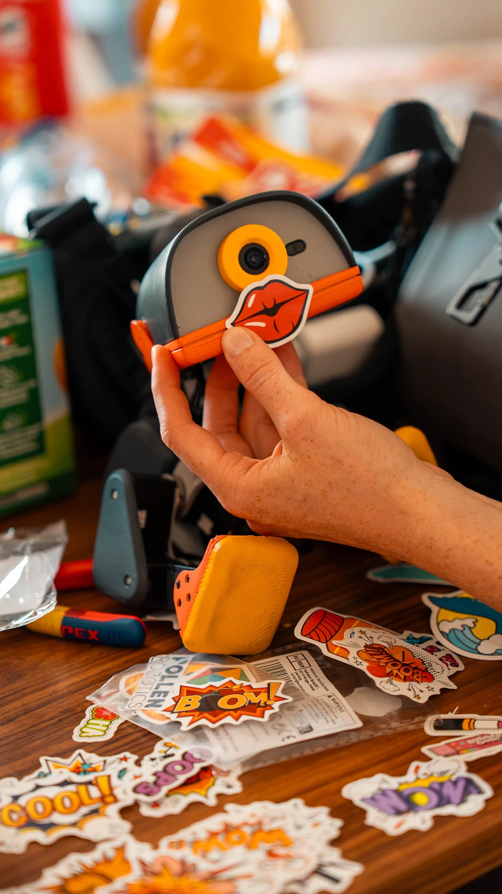 A red lips sticker is being placed on a Graphite Microduck’s beak, with more stickers lying nearby.