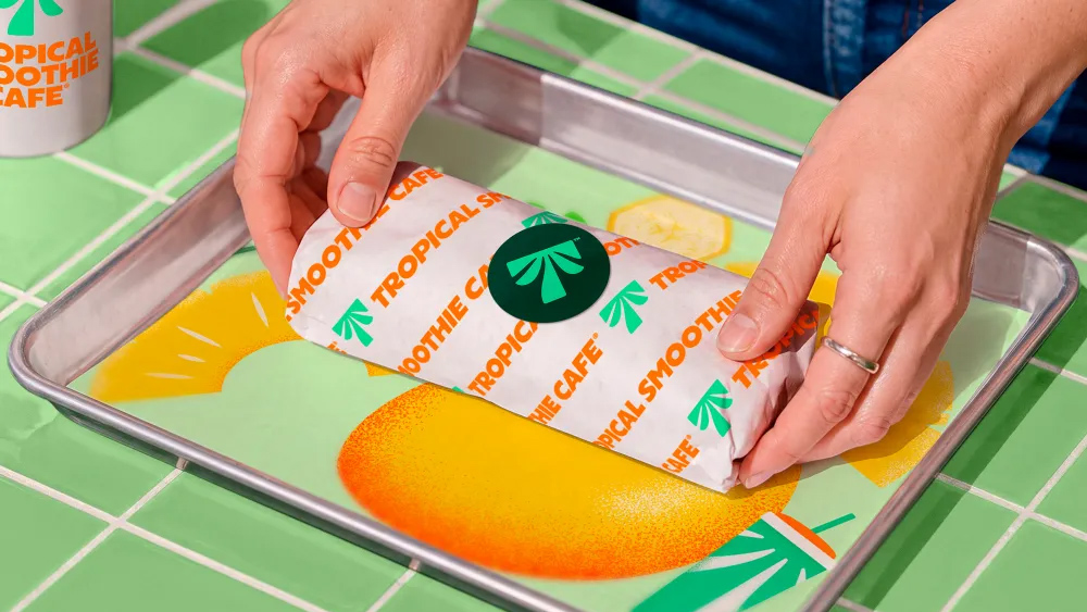 A wrap in paper patterned with orange Tropical Smoothie Cafe lettering and green palms