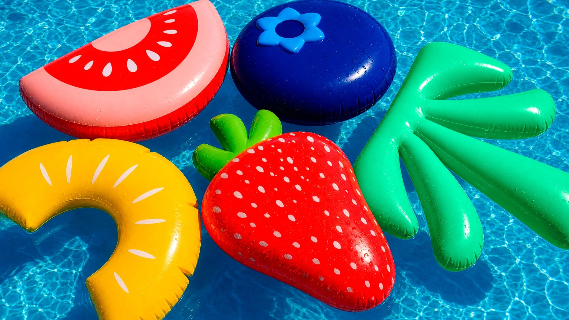 An inflatable green palm and fruit shapes floating in a blue swimming pool