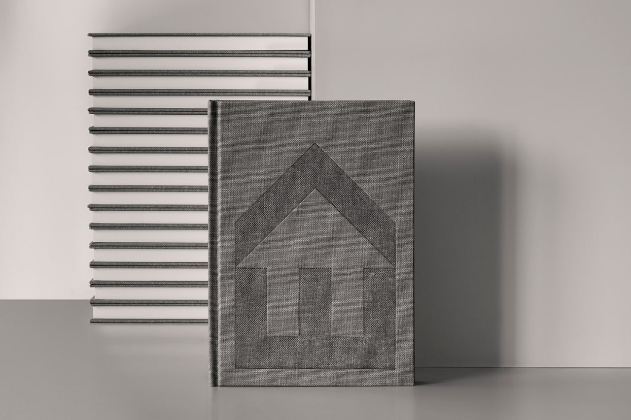 A grey cloth-covered notebook with a large embossed Enter Arkitektur mark, standing in front of stacked notebooks.